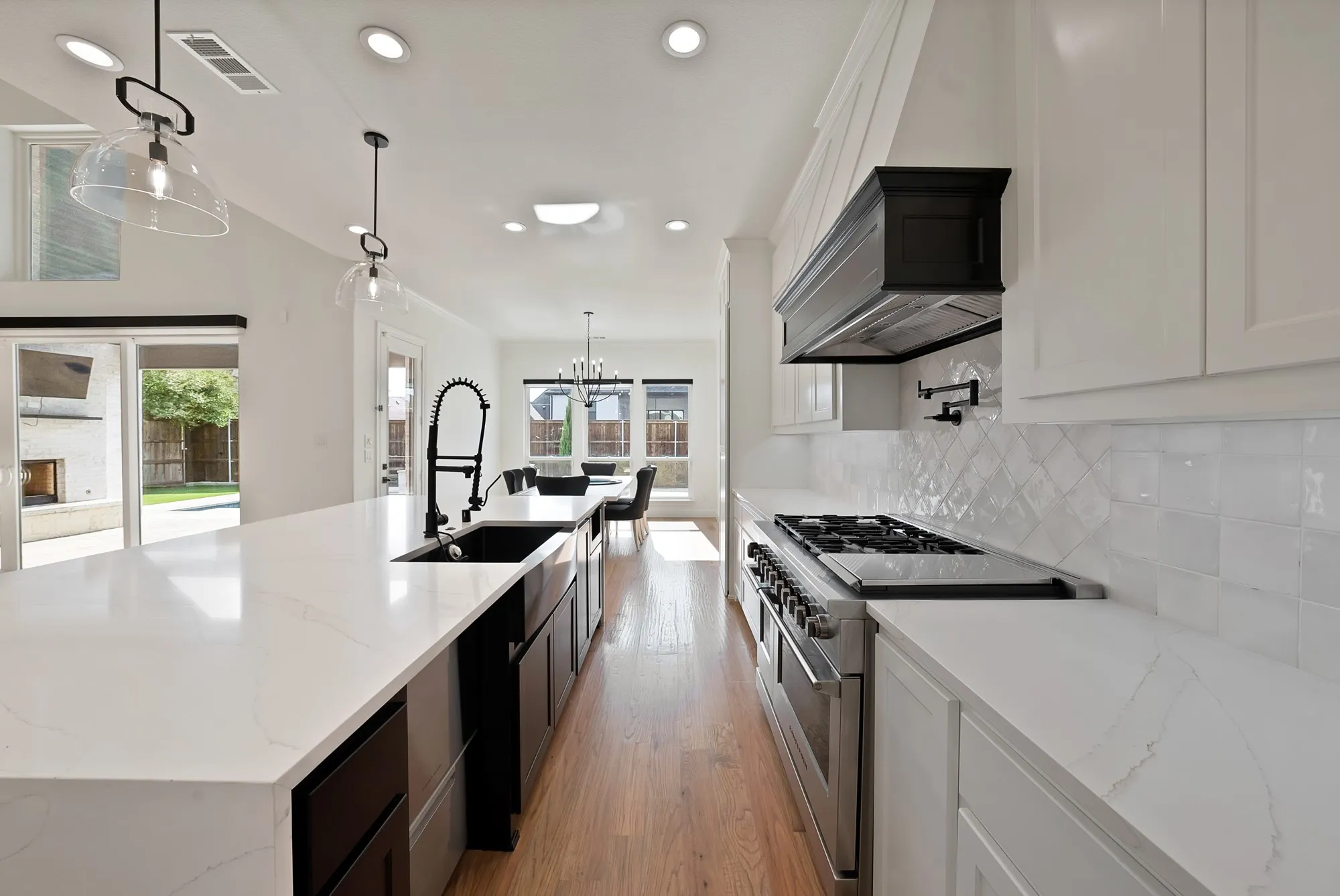 Expansive quartz countertops, wood-finish flooring, white cabinetry, a stainless steel range, and a built-in kitchen hood