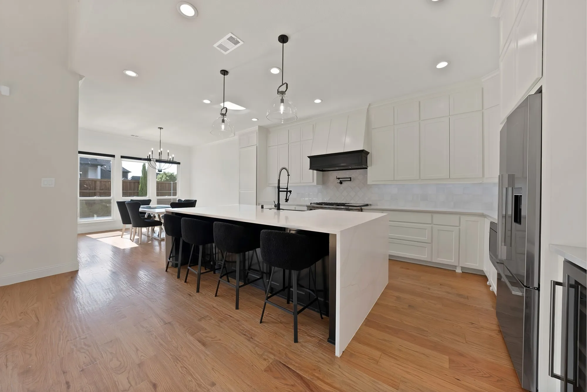 Spacious kitchen featuring an expansive island with seating, pendant lighting, built-in stainless steel appliances, and wood-finish flooring