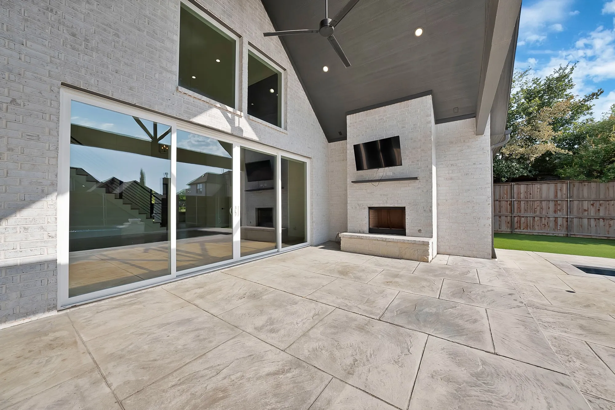 Expansive patio featuring large format pavers, a built-in fireplace with a stone hearth, and a covered ceiling with recessed lighting and a ceiling fan