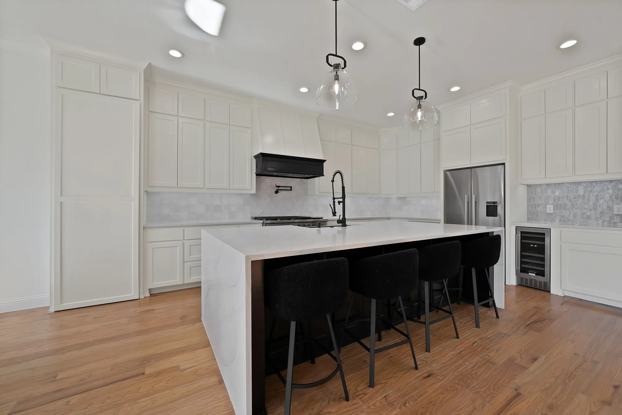 Kitchen featuring light wood-finish flooring, white perimeter cabinetry, stainless steel appliances, a paneled refrigerator, and a kitchen island with seating