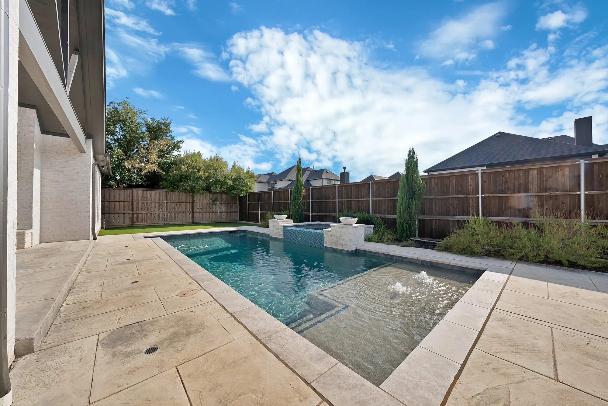 Outdoor living space featuring a swimming pool, integrated spa with fountains, and expansive stone paving