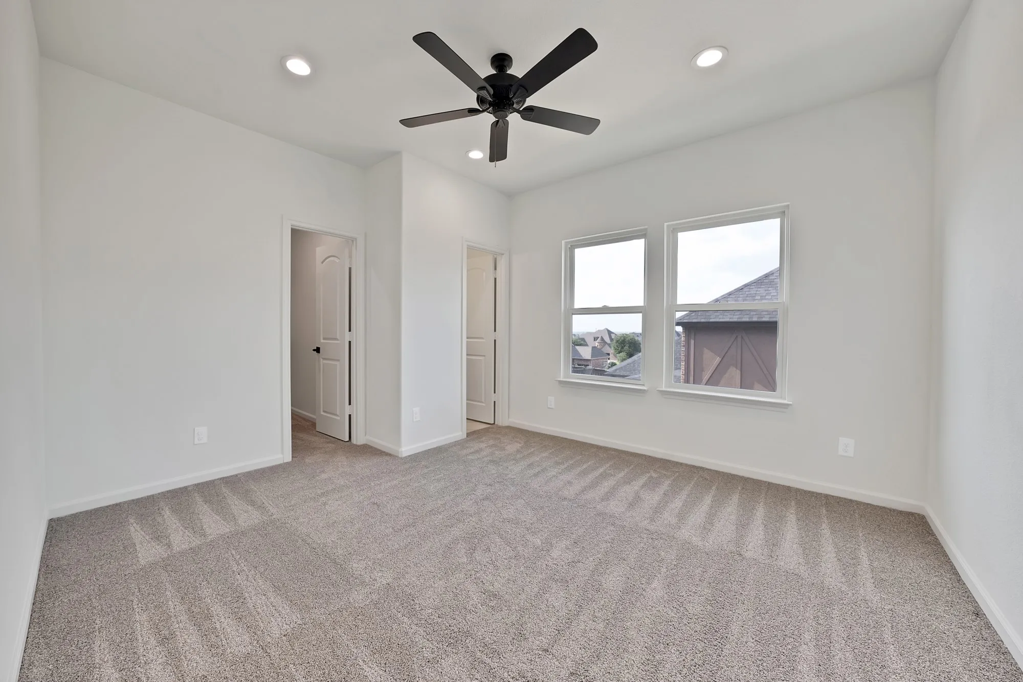 Neutral-toned carpeting, white walls, two windows, recessed lighting, and a ceiling fan