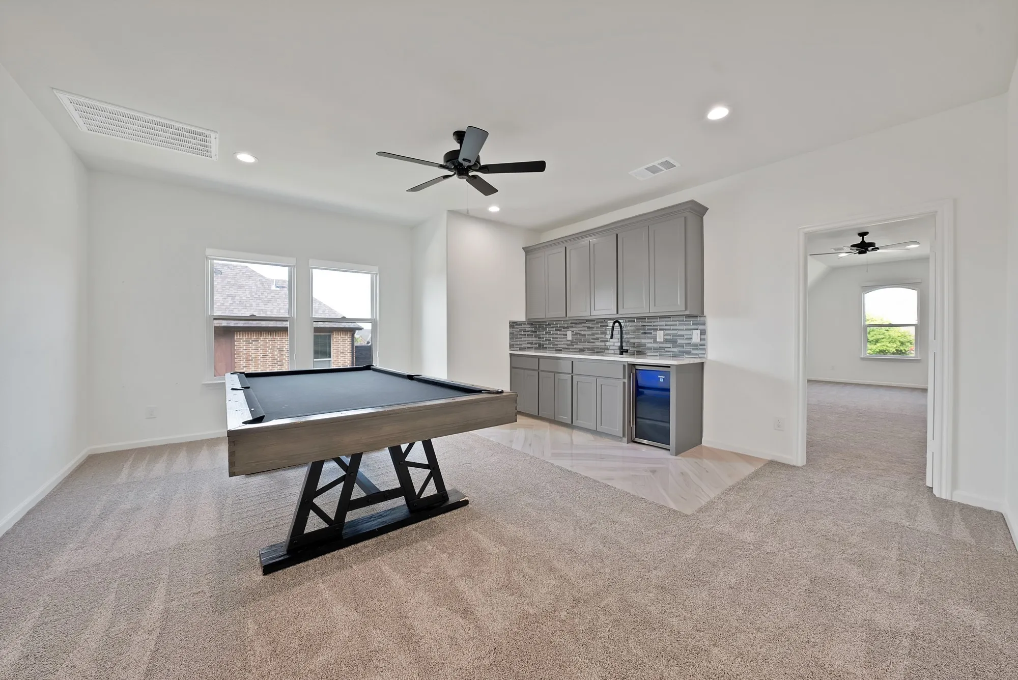 Spacious room with recessed lighting, ceiling fan, dual windows, and built-in wet bar featuring a beverage cooler and tiled backsplash