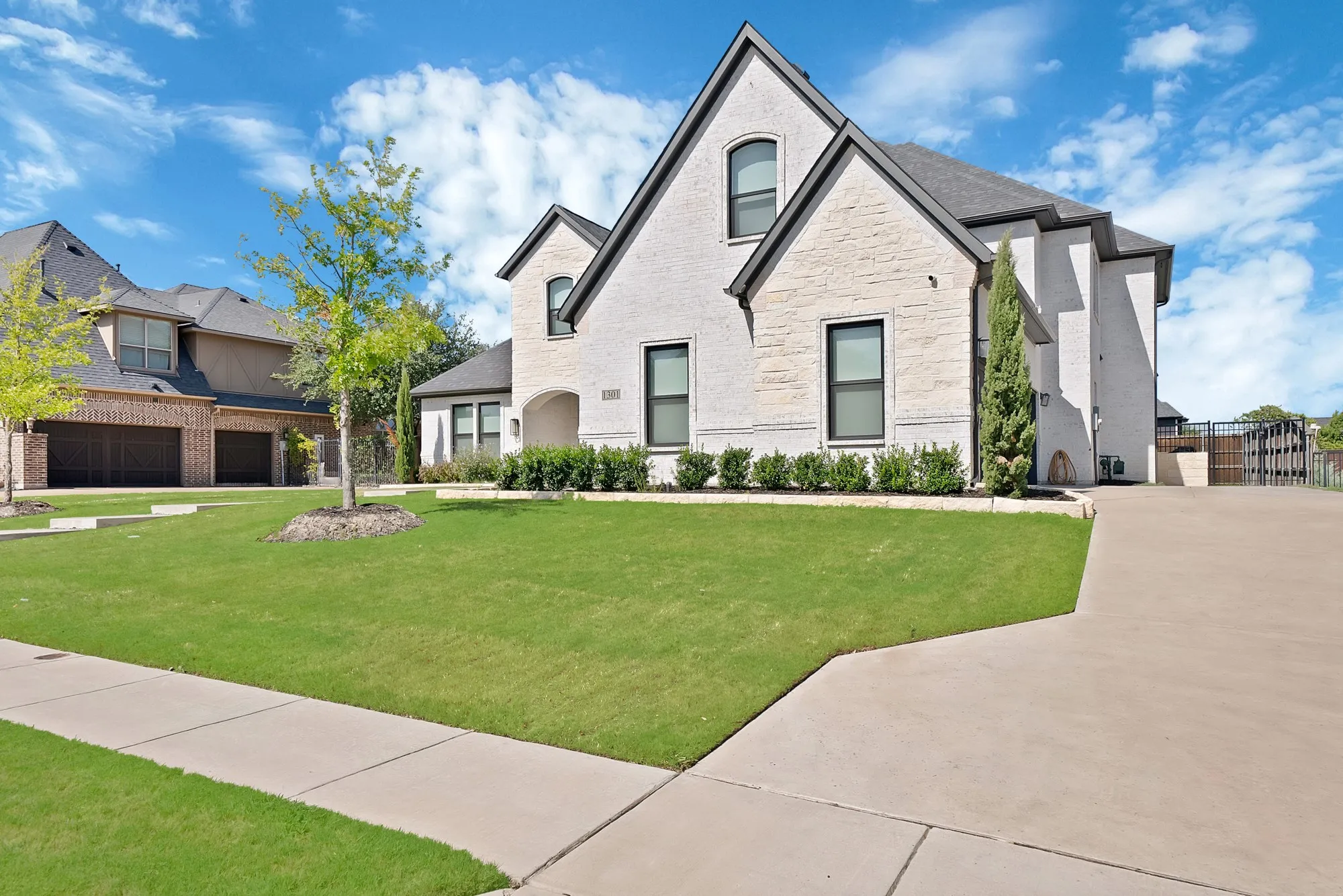 Stone and stucco exterior with dark trim windows, front yard with mature landscaping, and a concrete driveway