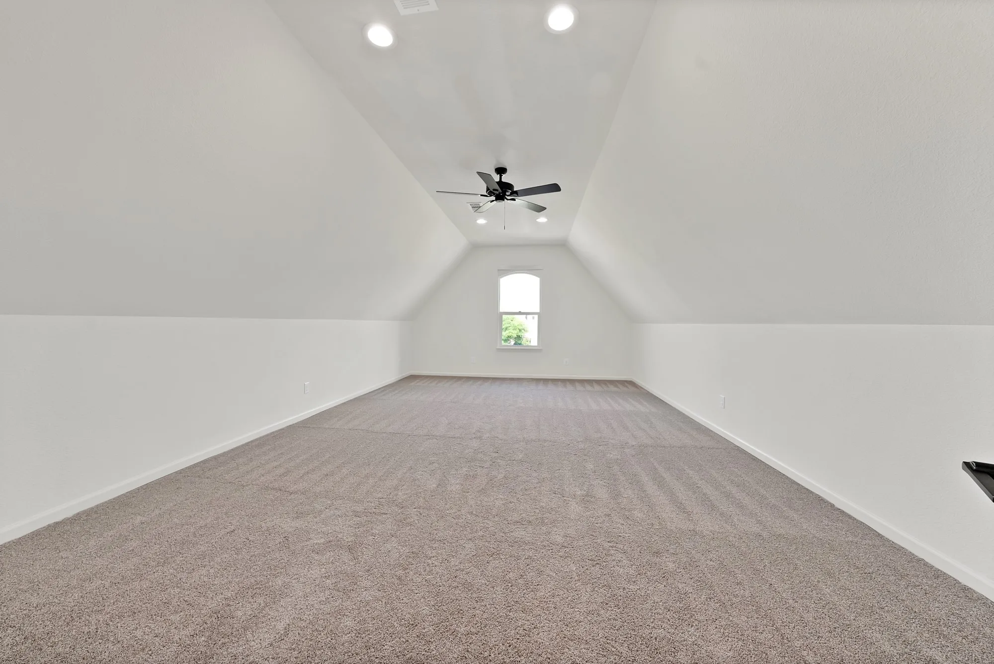 Expansive carpeted room featuring a vaulted ceiling with recessed lighting, a ceiling fan, and an arched window