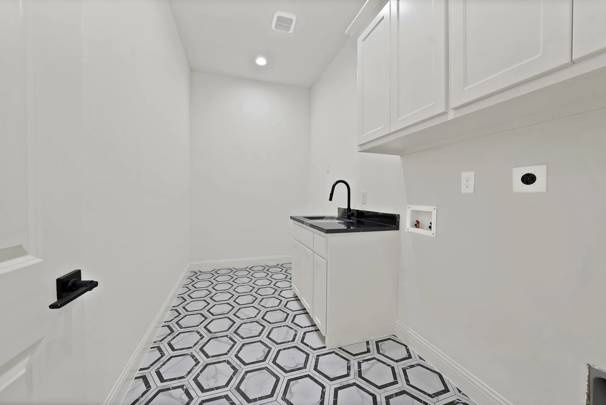 Hexagonal floor tiling, white cabinetry, undermount sink, dark countertop, and matte black faucet