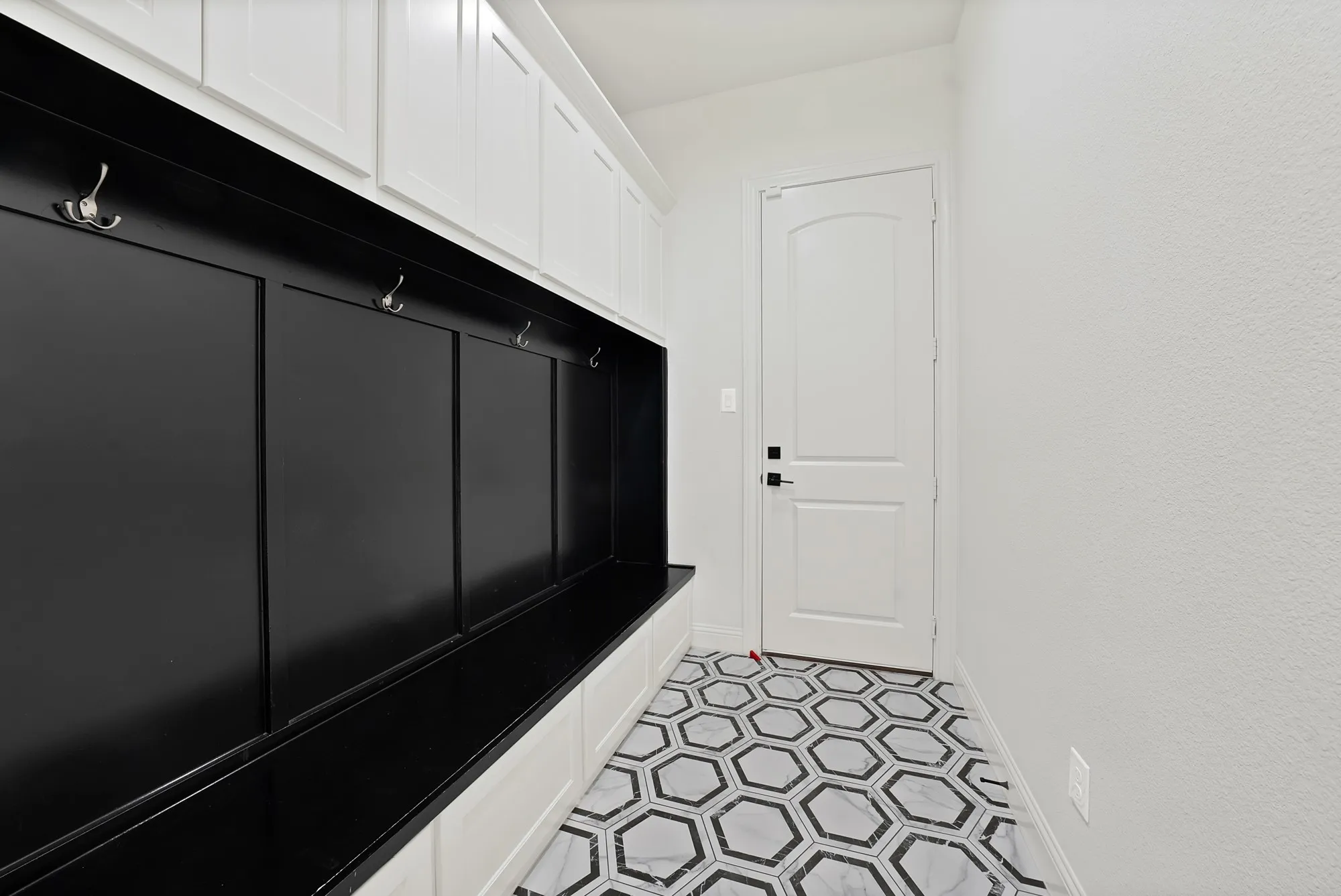 Modern hallway featuring geometric hexagonal tile flooring in gray and white tones, sleek white paneled door with contemporary hardware, crisp white walls, and recessed lighting throughout