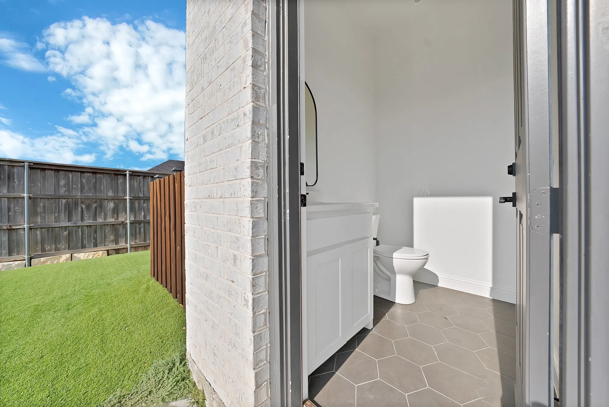 White brick exterior, artificial turf lawn, privacy fencing, hexagonal floor tiles, white vanity with integrated sink