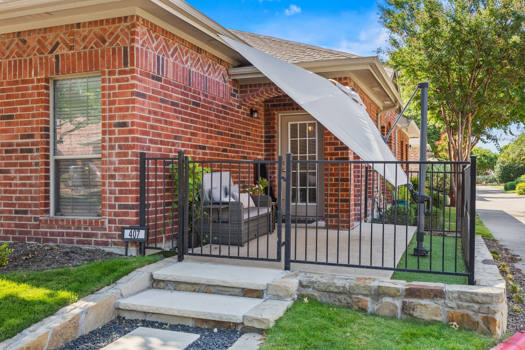 Brick exterior with decorative detailing, stone retaining wall, and black metal fencing enclosing a patio area