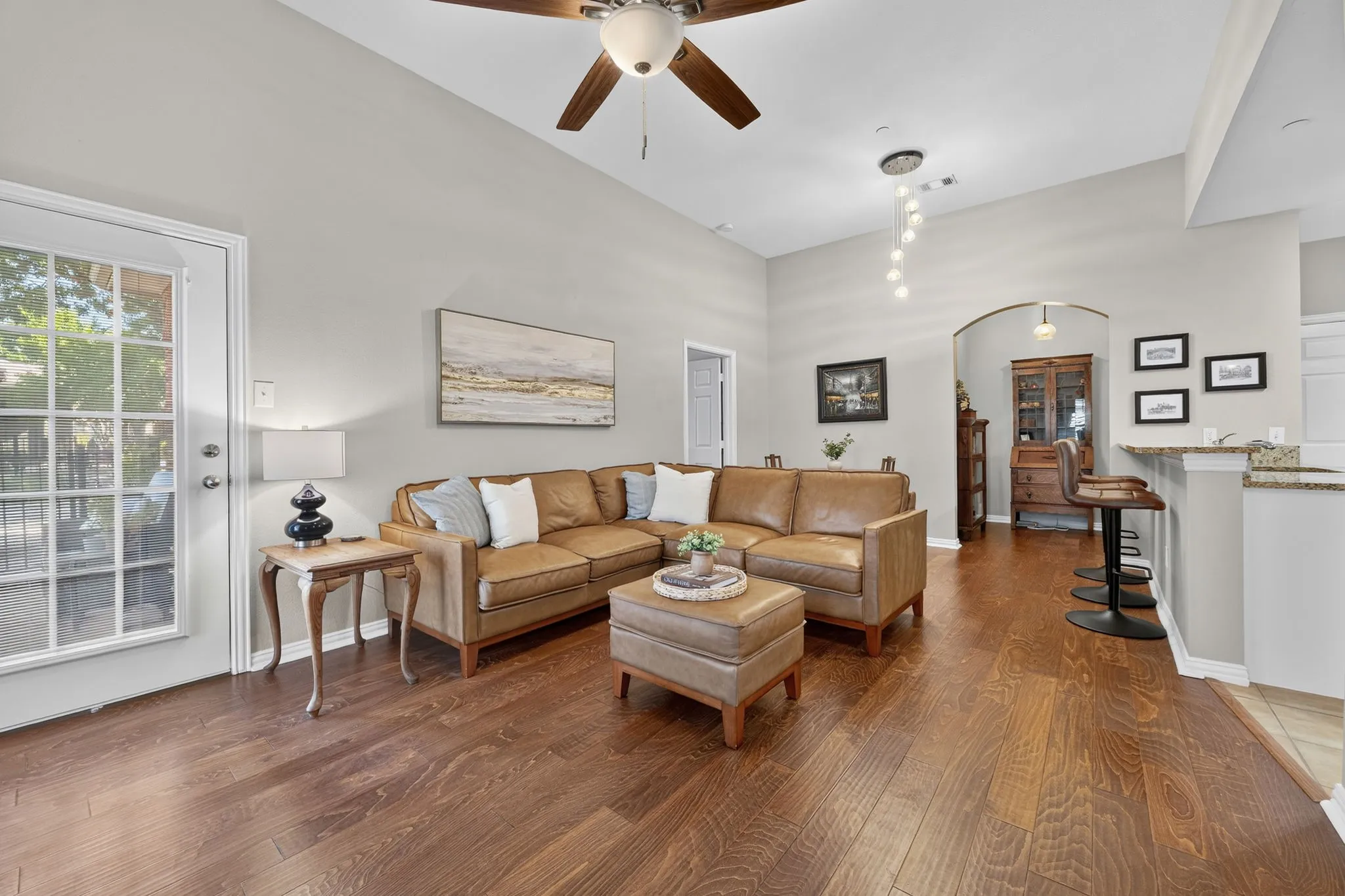 Varnished wood-finish flooring, vaulted ceiling with a ceiling fan, arched entryway, and a breakfast bar with stone-finish countertops