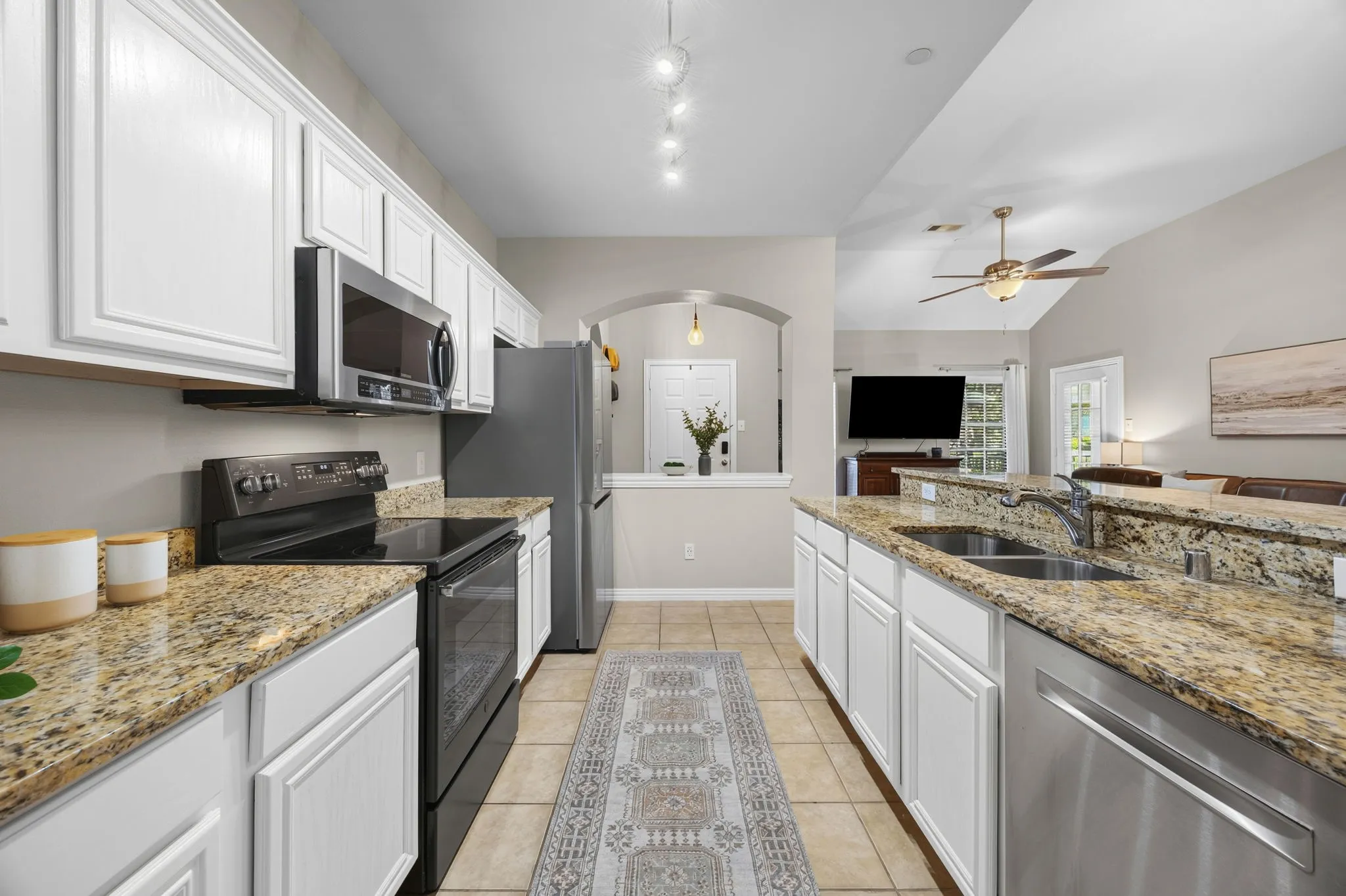 Kitchen featuring granite countertops, white cabinetry, stainless steel appliances, tile flooring, and an arched doorway