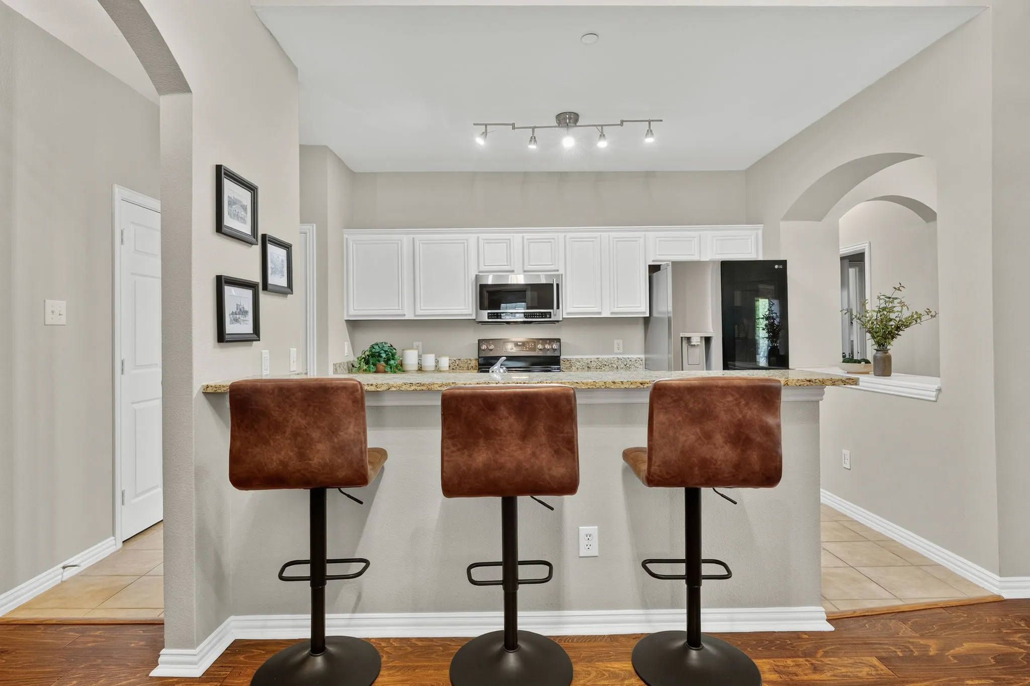Kitchen featuring white cabinetry, stainless steel appliances, granite countertops, a breakfast bar, and track lighting