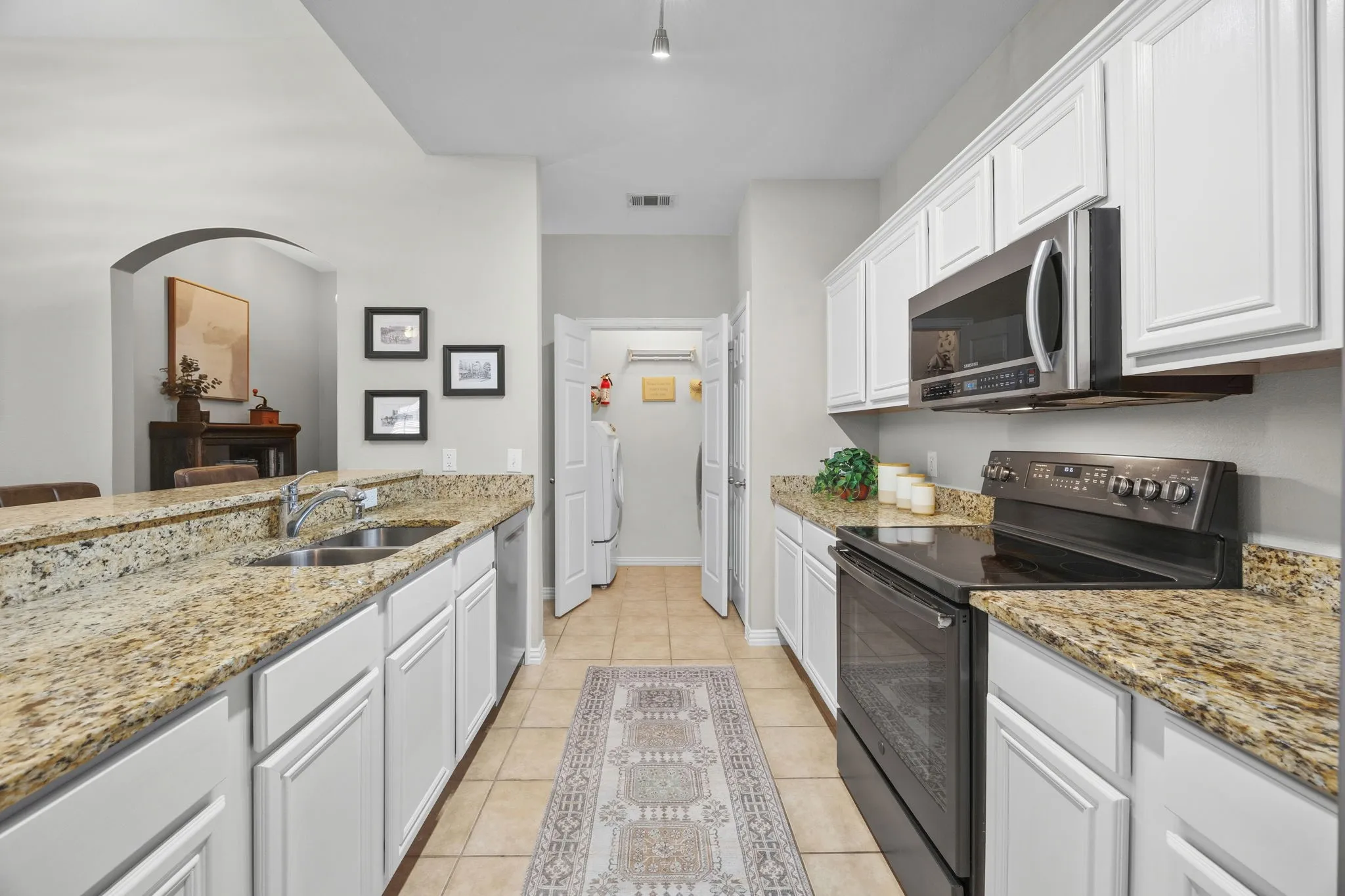Kitchen featuring white cabinetry, granite countertops, tile flooring, a stainless steel double basin sink, and a built-in microwave