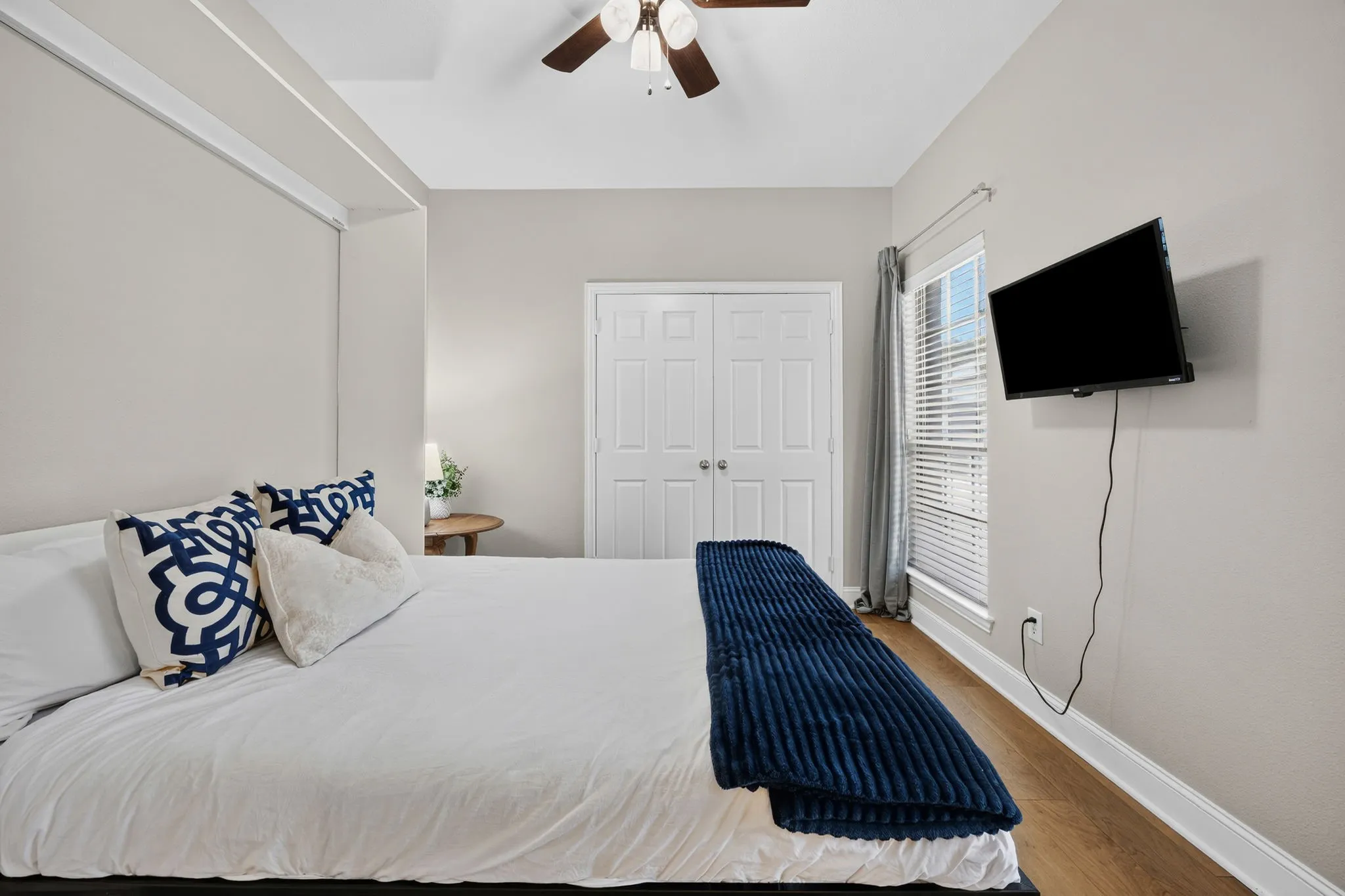 Hardwood-finish flooring, ceiling fan, window with blinds, and white bi-fold closet doors