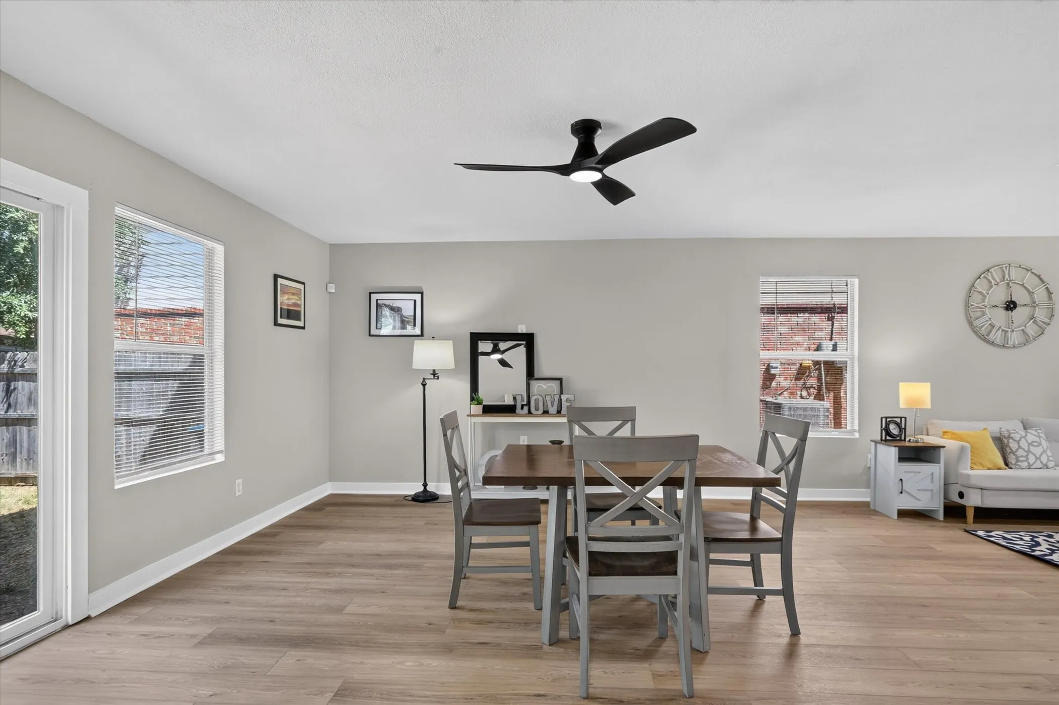 Wood-finish flooring, light gray wall paint, white trim, sliding glass patio door, and a ceiling fan with integrated lighting