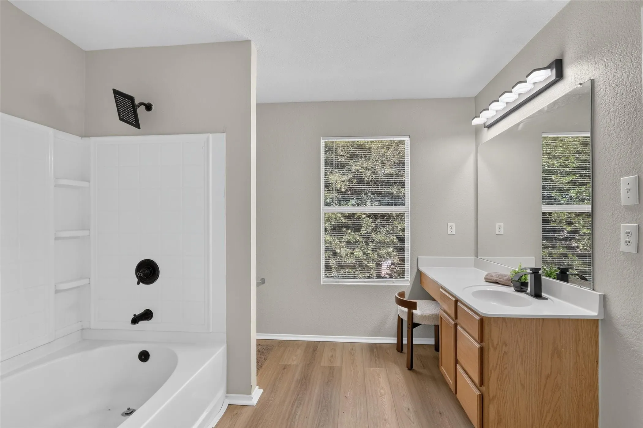 Bathroom featuring a white tub with matte black fixtures, an expansive vanity with a single sink and light wood-finish cabinetry, a large mirror, and wood-finish flooring