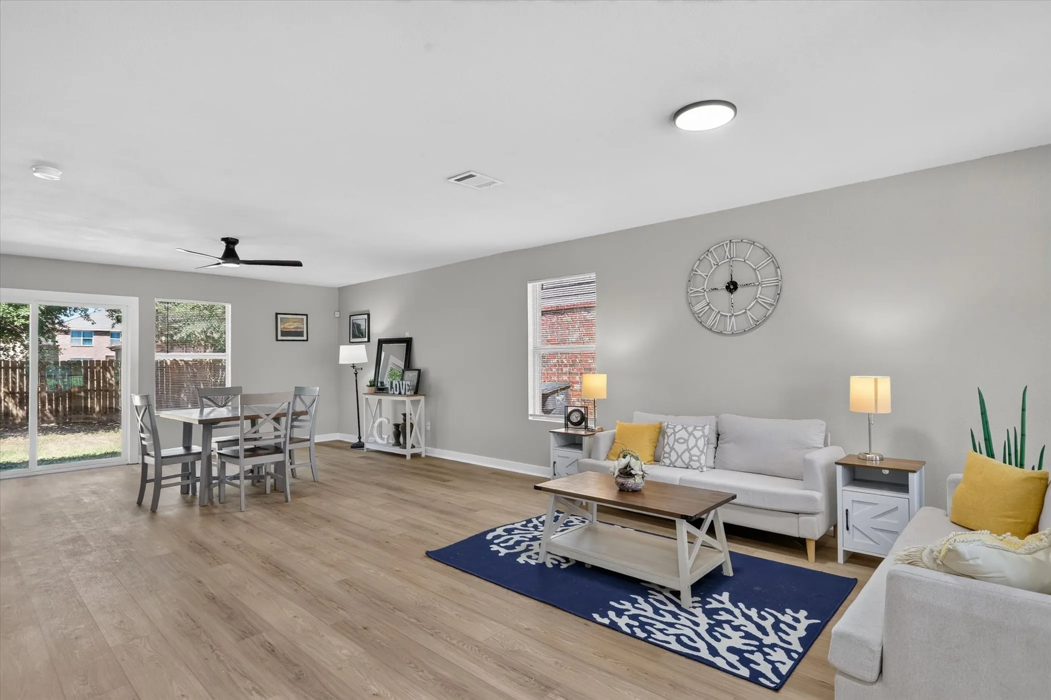 Expansive open-concept living area featuring wood-finish flooring, neutral gray walls, a ceiling fan, and sliding glass doors to the exterior