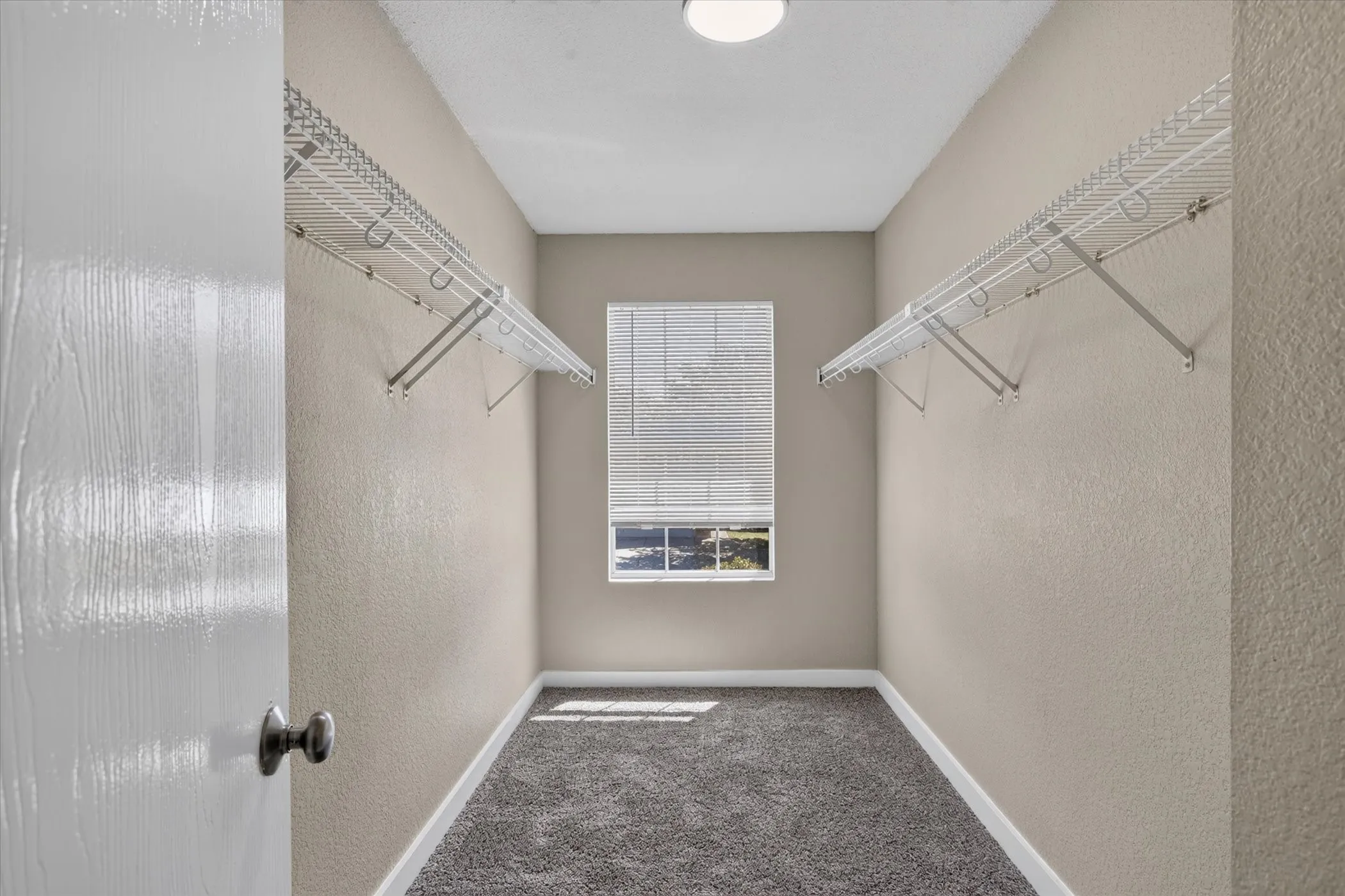 Recessed lighting, window with blinds, wall-mounted wire shelving, and dark gray carpeting