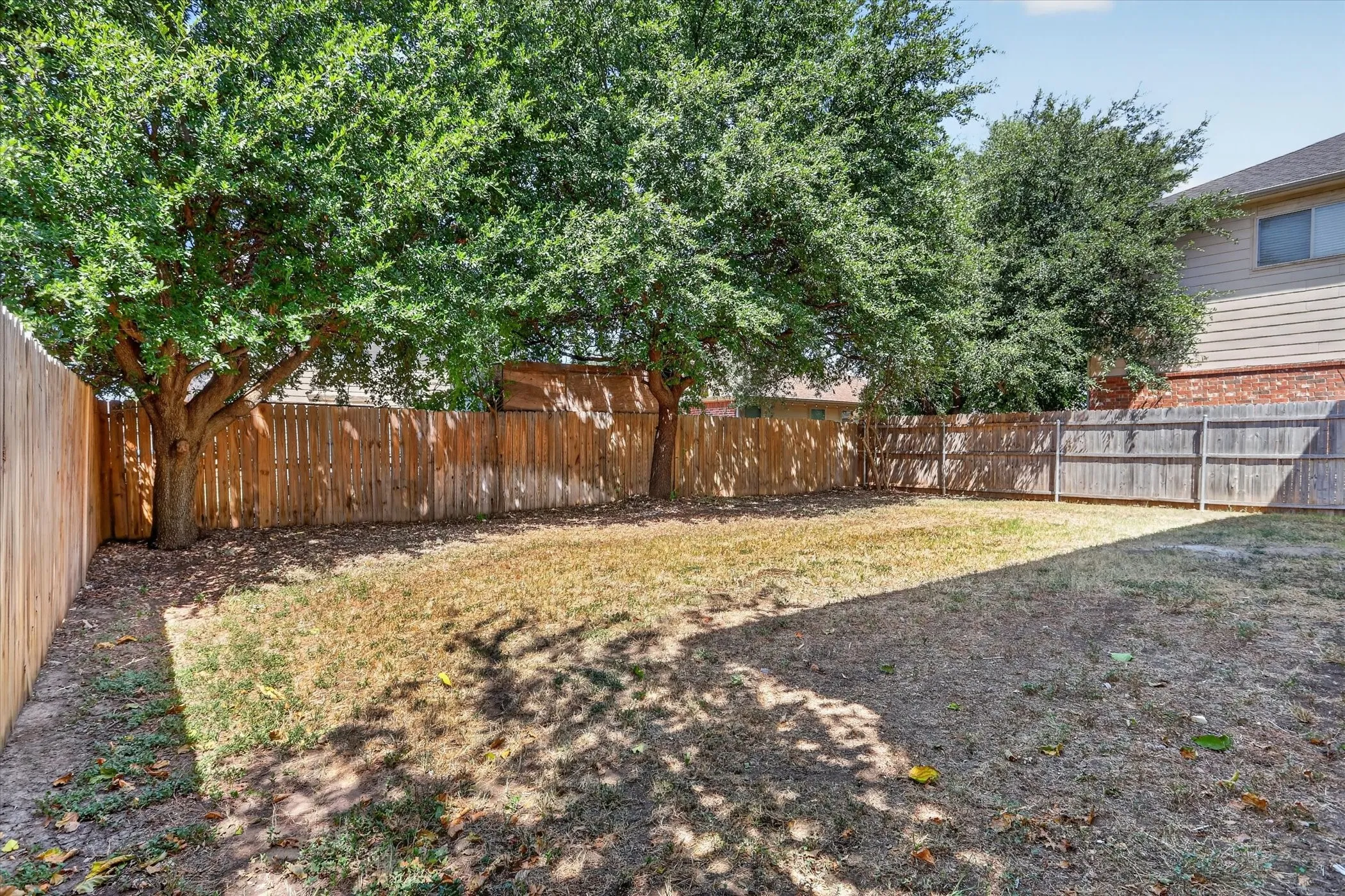 Spacious backyard featuring wood-panel fencing, mature trees, and an expansive lawn area