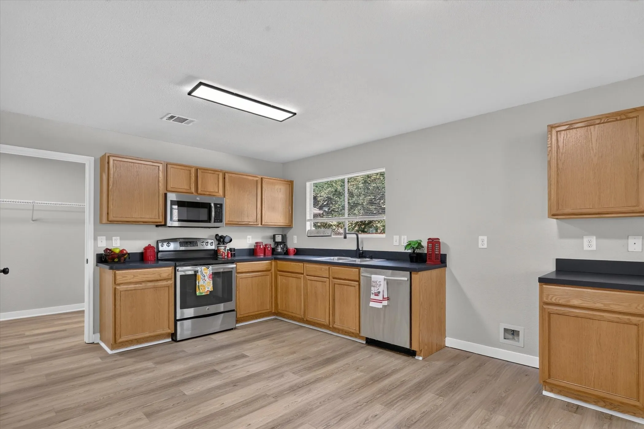 Kitchen featuring wood-finish flooring, wood cabinetry, dark countertops, stainless steel appliances, and a window