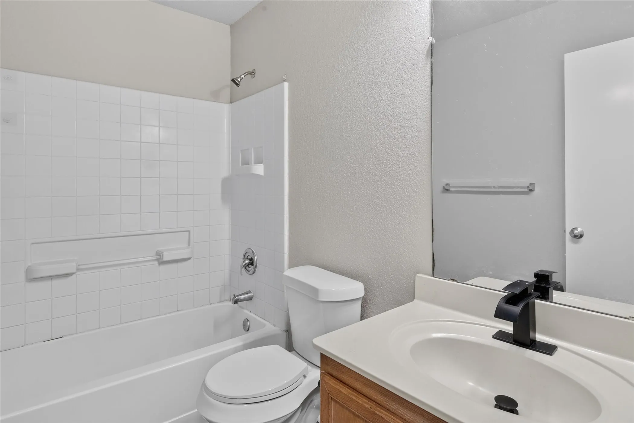 White subway tile shower surround with integrated soap dishes, a white bathtub, and a modern black faucet