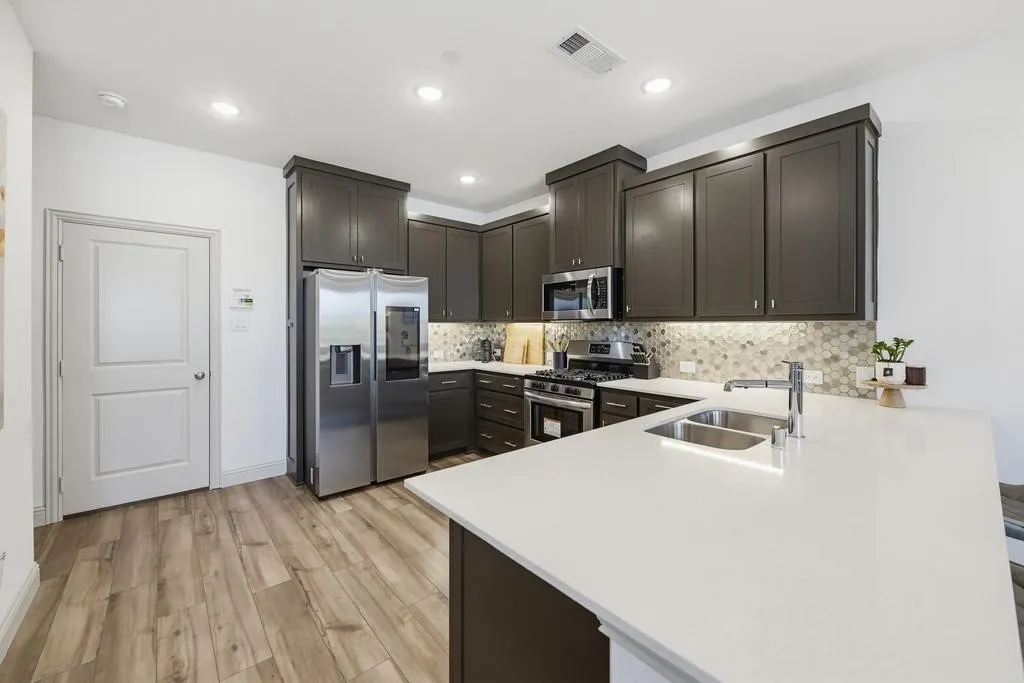 White quartz countertop island with an undermount sink and a polished chrome faucet, dark wood-finish cabinetry, stainless steel appliances, and wood-finish flooring