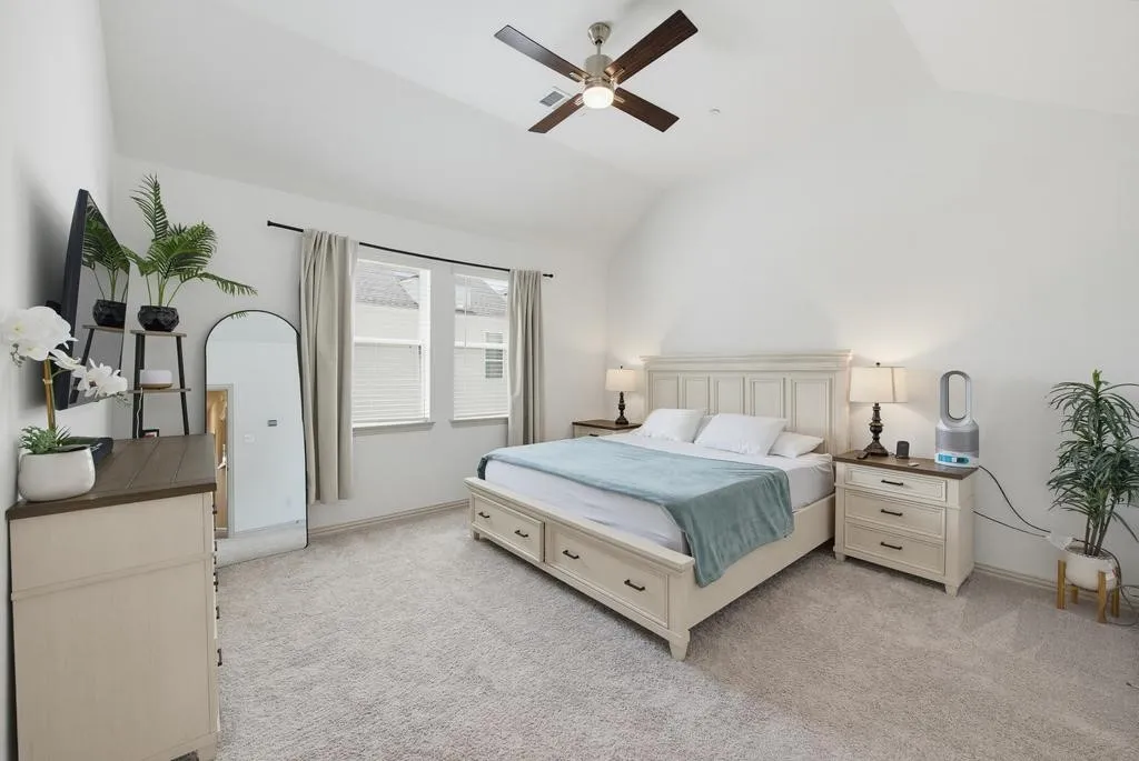 Vaulted ceiling, ceiling fan with light fixture, carpeted flooring, and two windows