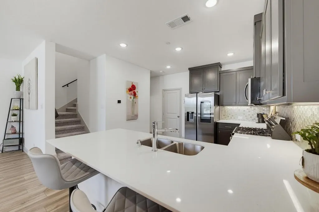 Kitchen island with an undermount double-basin sink, stainless steel appliances, grey cabinetry, and a patterned tile backsplash