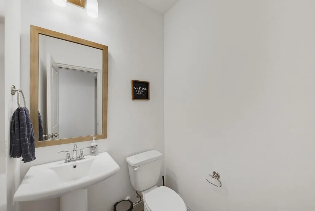 Pedestal sink with chrome-finish faucet, rectangular wood-frame mirror, and wall-mounted light fixture