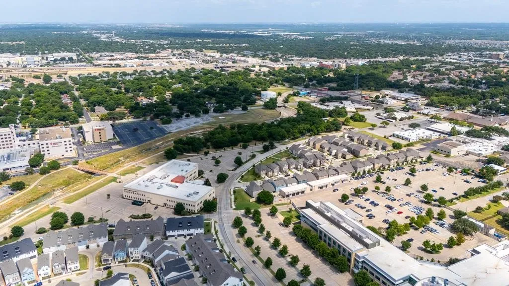 Aerial perspective of a developed urban landscape featuring diverse building types, established trees, and extensive paved areas