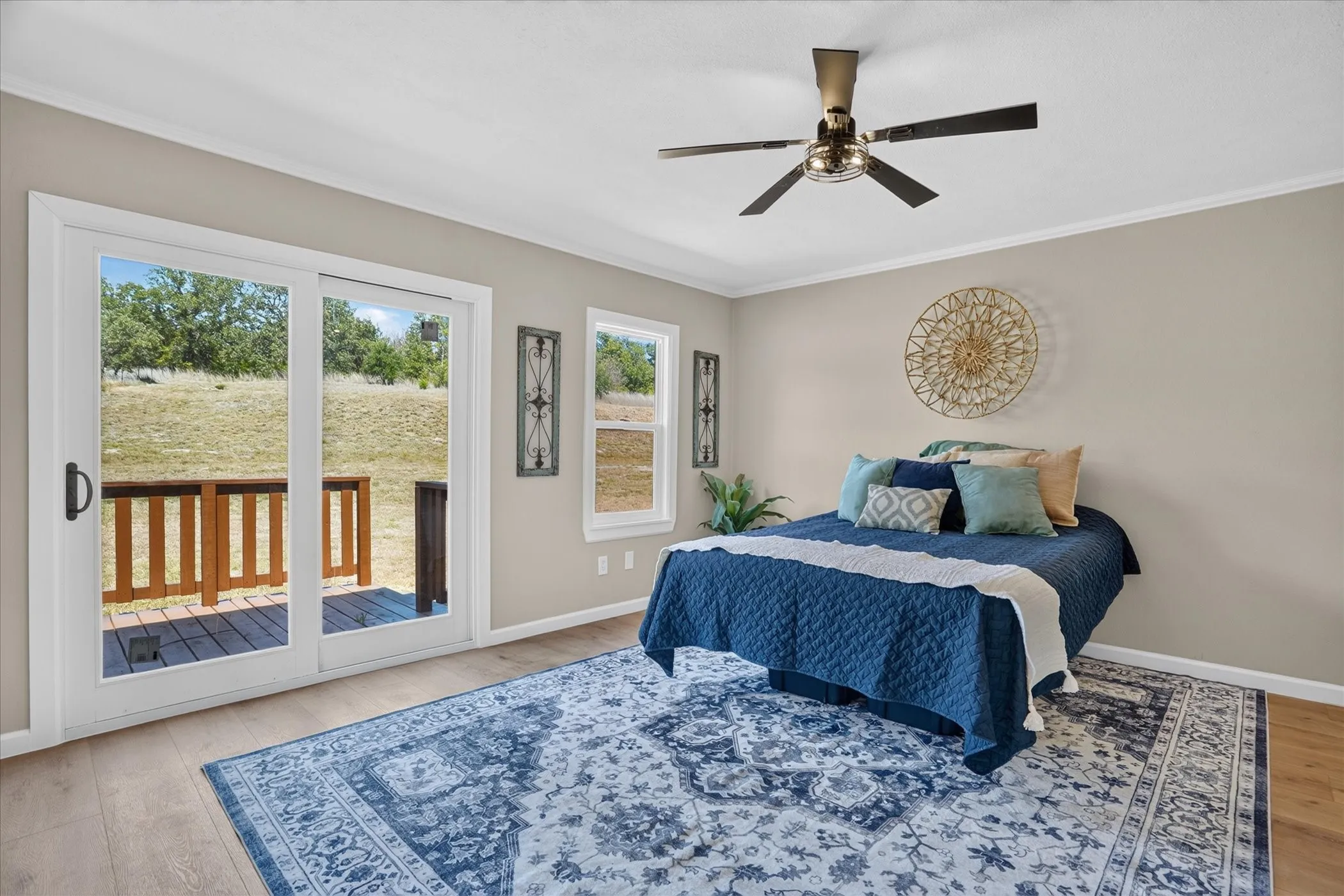 Wood-finish flooring, ceiling fan with integrated lighting, sliding glass door to exterior deck, and large window