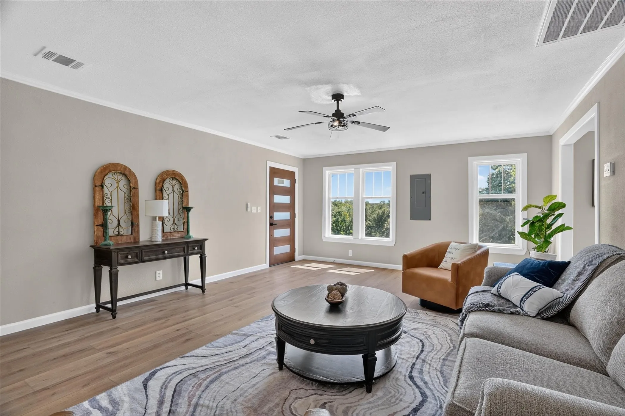 Spacious living area featuring wood-finish flooring, a ceiling fan, and multiple windows