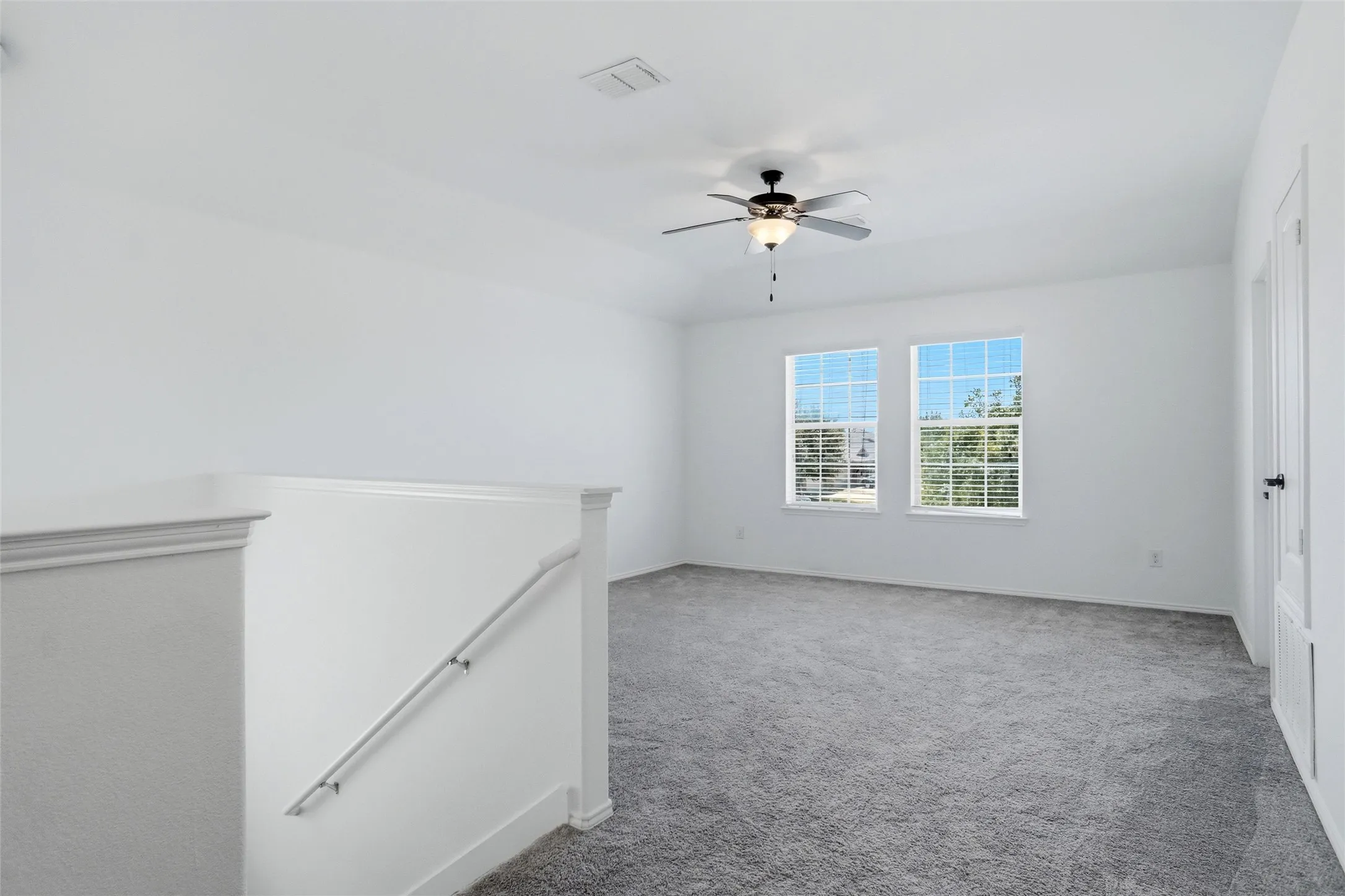 Upper level bonus room featuring two windows with horizontal blinds, a ceiling fan, and carpeted flooring