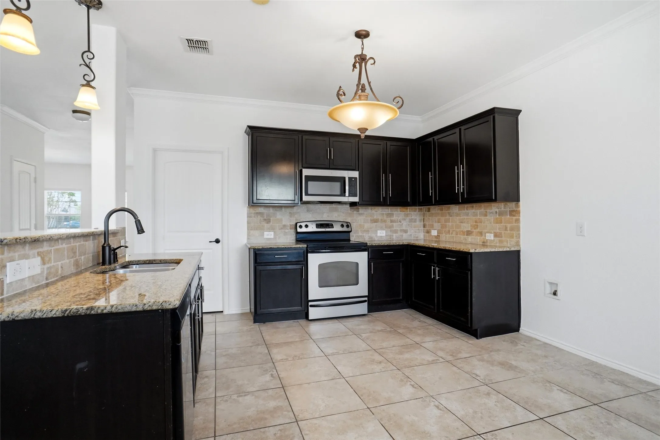 Kitchen featuring dark-finish cabinetry, stainless steel appliances, a light-toned tile backsplash, and a granite-finish countertop with an undermount sink