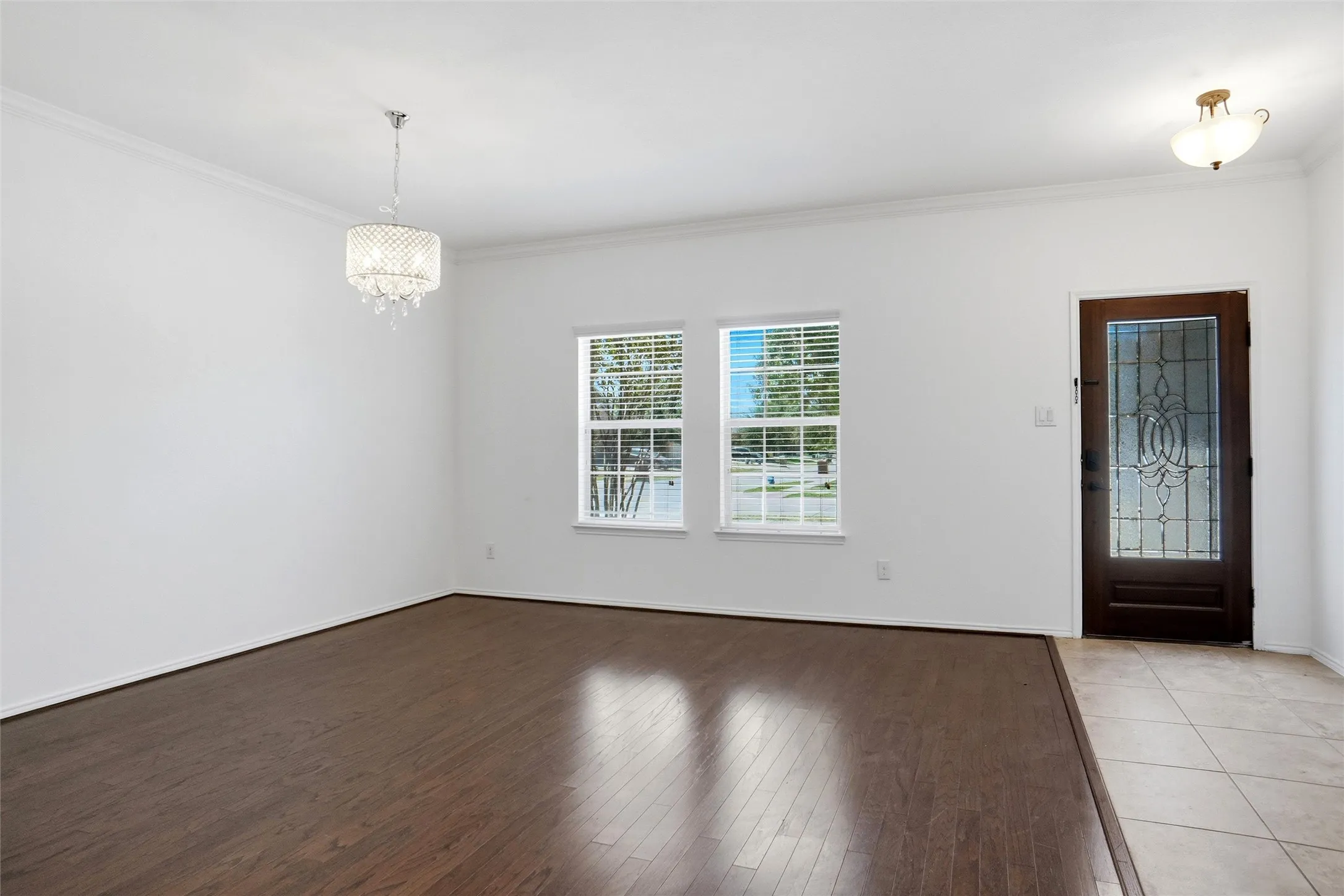 Wood-finish flooring, white walls, decorative chandelier, transom window, and tiled entry