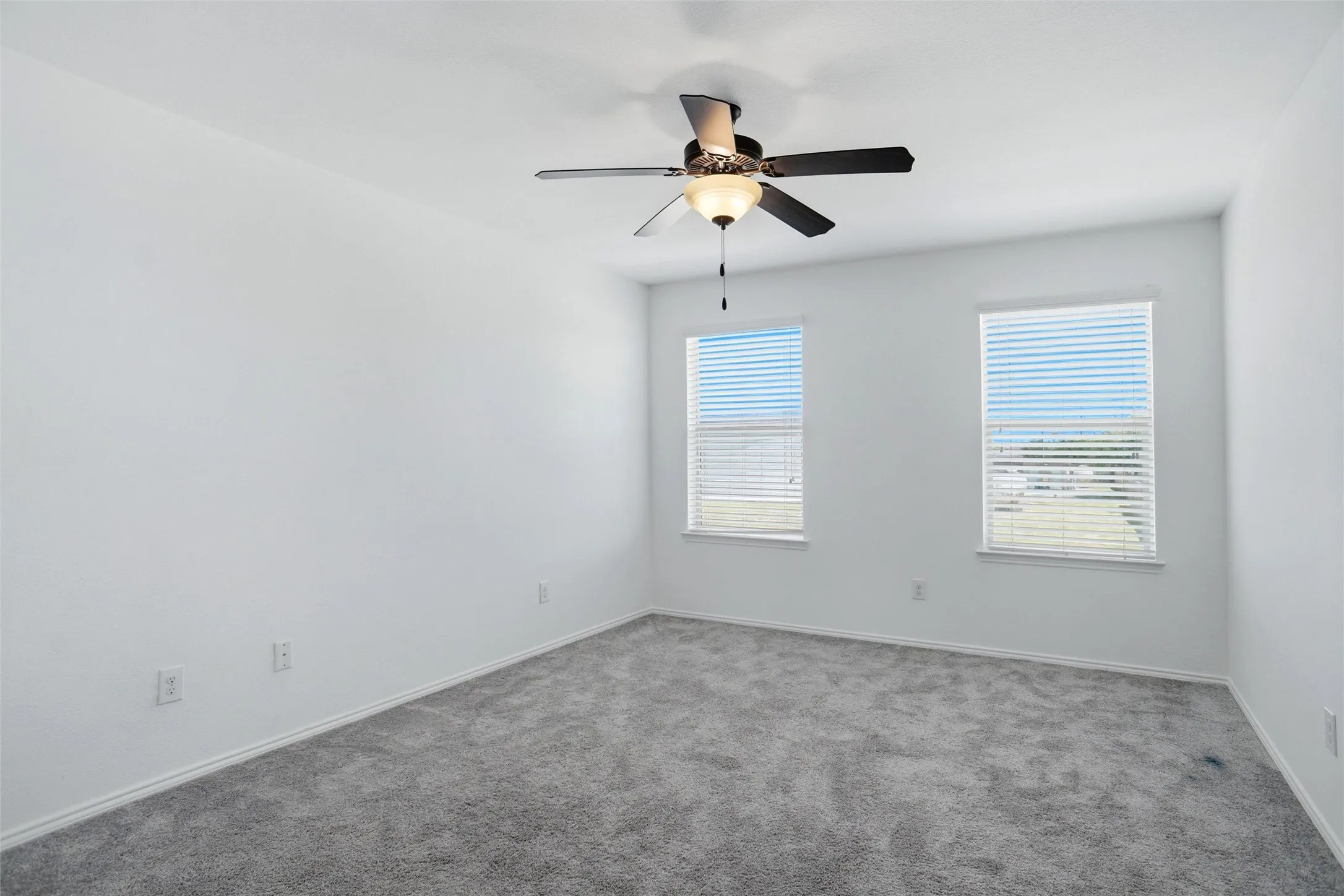 Room featuring two windows with blinds, gray carpet, and a ceiling fan with integrated lighting