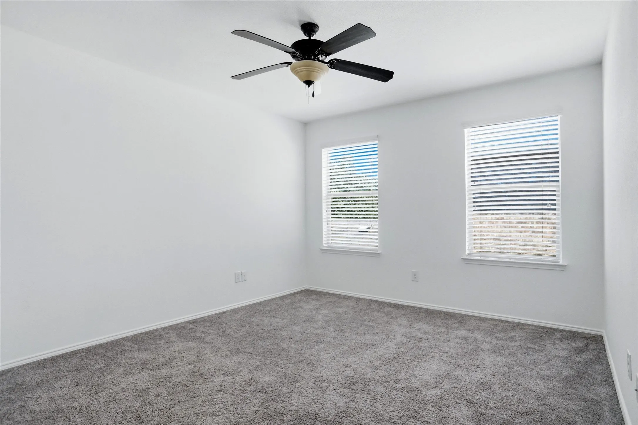 Recessed windows with blinds, ceiling fan, and grey carpet flooring