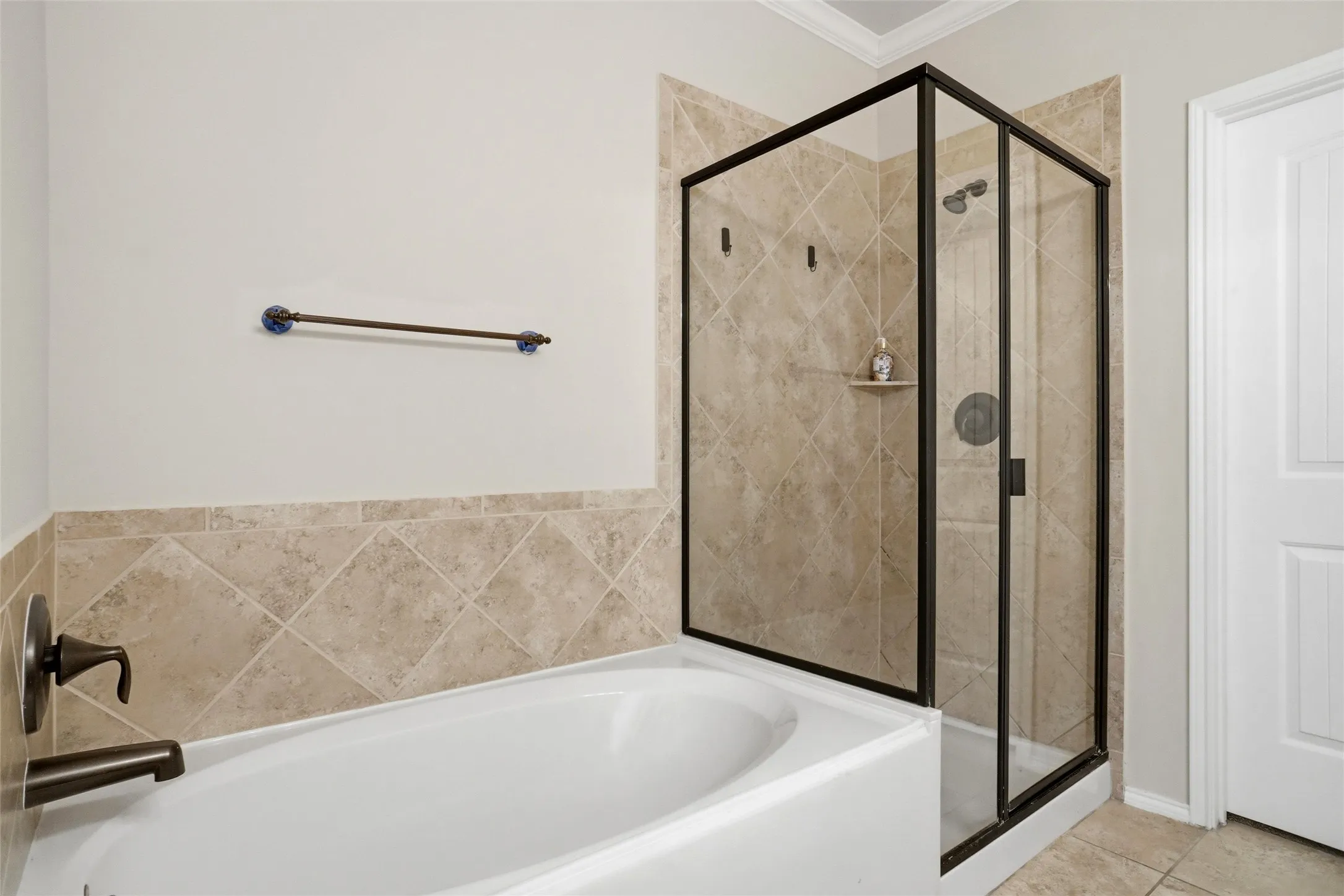 White bathtub with bronze-finish fixtures, a separate shower with black-framed glass enclosure, and tiled walls with diagonal pattern