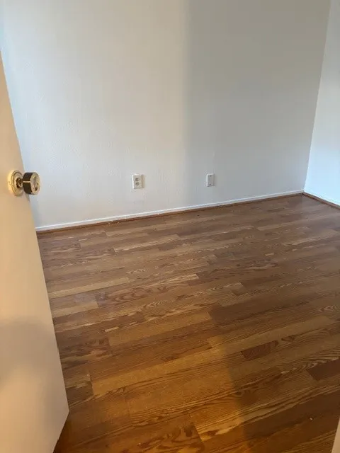 Spare room with dark wood-type flooring and baseboards