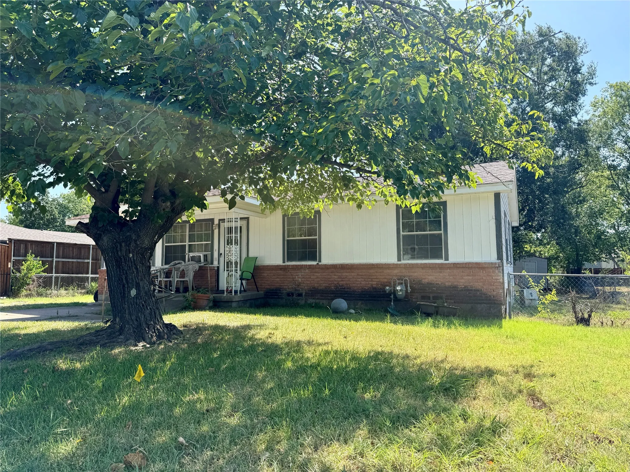 Exterior featuring white siding, brick foundation, and a mature tree