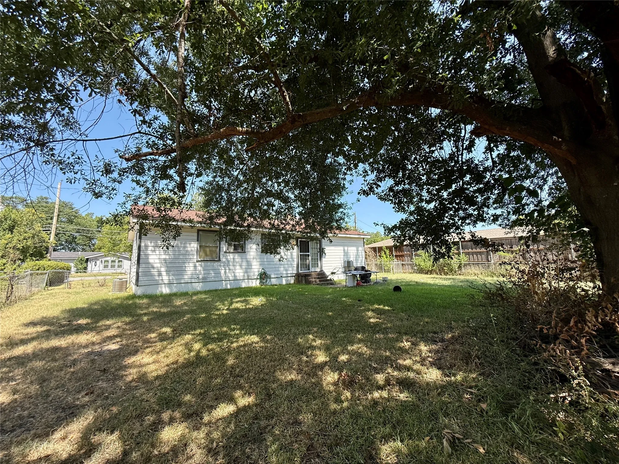 Expansive backyard featuring a mature tree canopy, chain-link fencing, and a white-sided residence