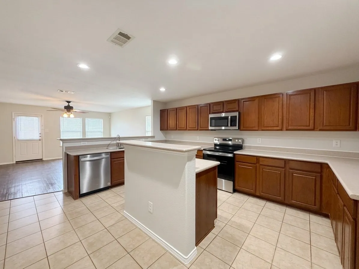 Kitchen featuring tile flooring, stainless steel appliances, wood-finish cabinetry, and light-toned countertops