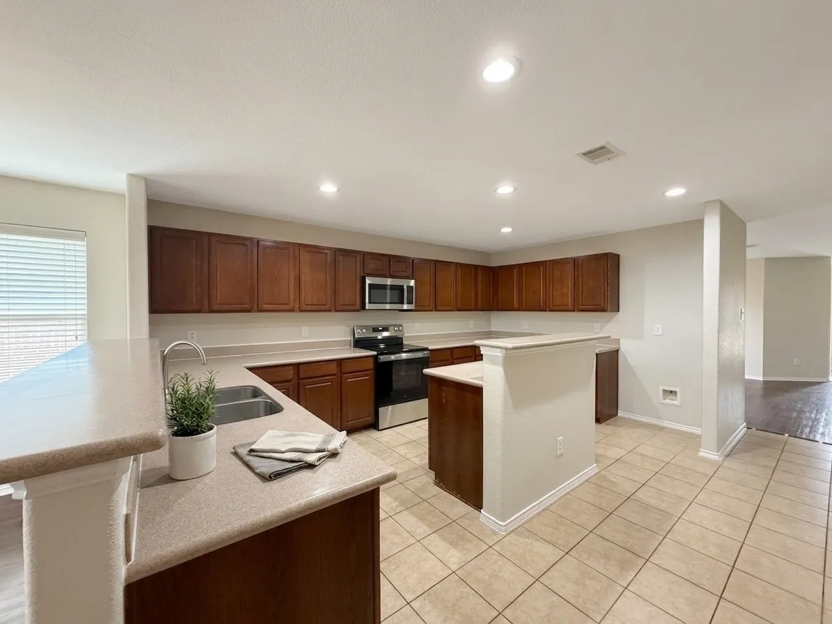 Kitchen featuring wood cabinetry, stainless steel appliances, a double basin sink, and tile flooring