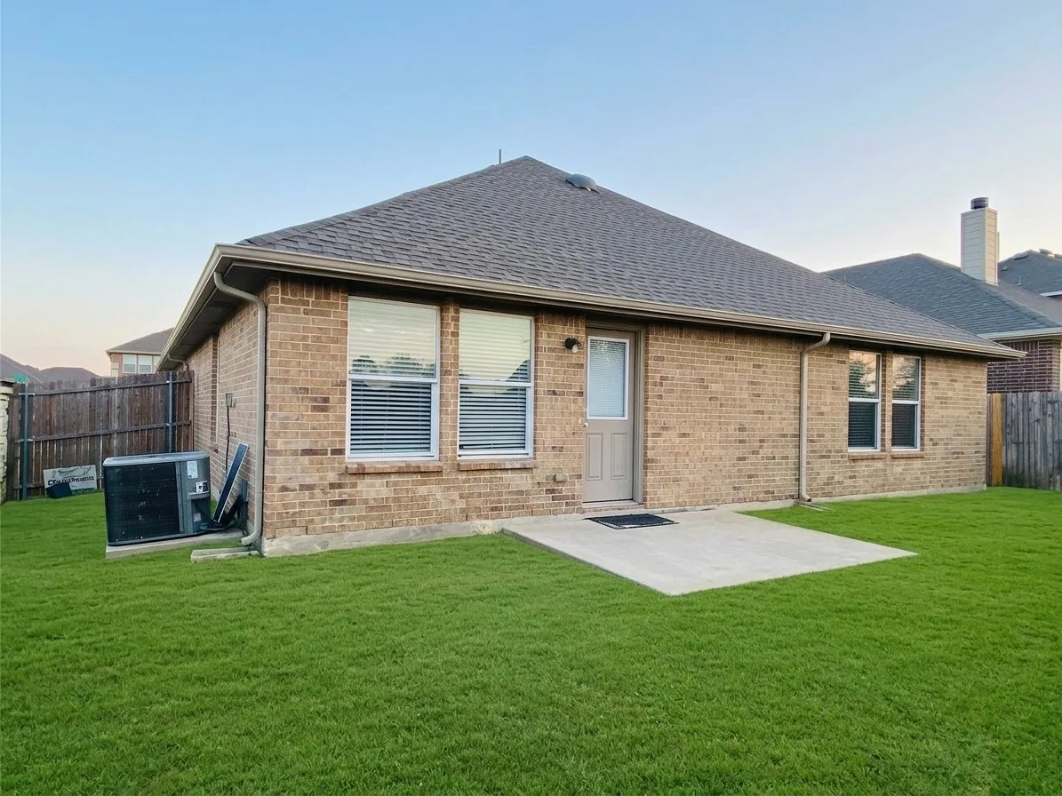 Expansive backyard featuring a manicured lawn, brick exterior, concrete patio, and privacy fencing