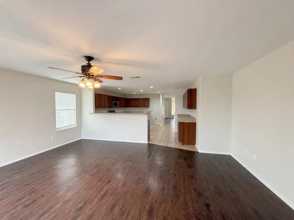 Wood-finish flooring throughout, ceiling fan with integrated lighting, kitchen featuring wood cabinetry, stainless steel microwave, and a breakfast bar