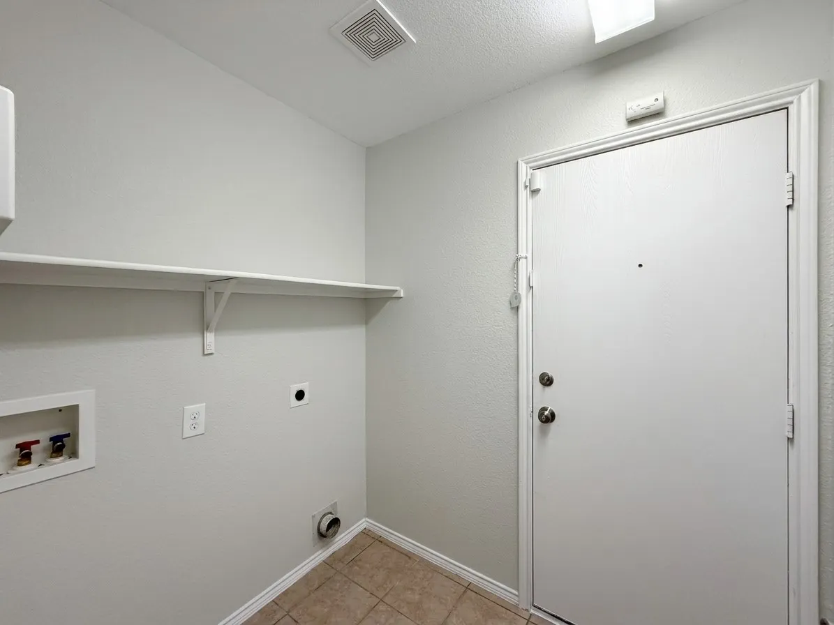 Utility space featuring a mounted storage shelf, tile flooring, and a white entry door