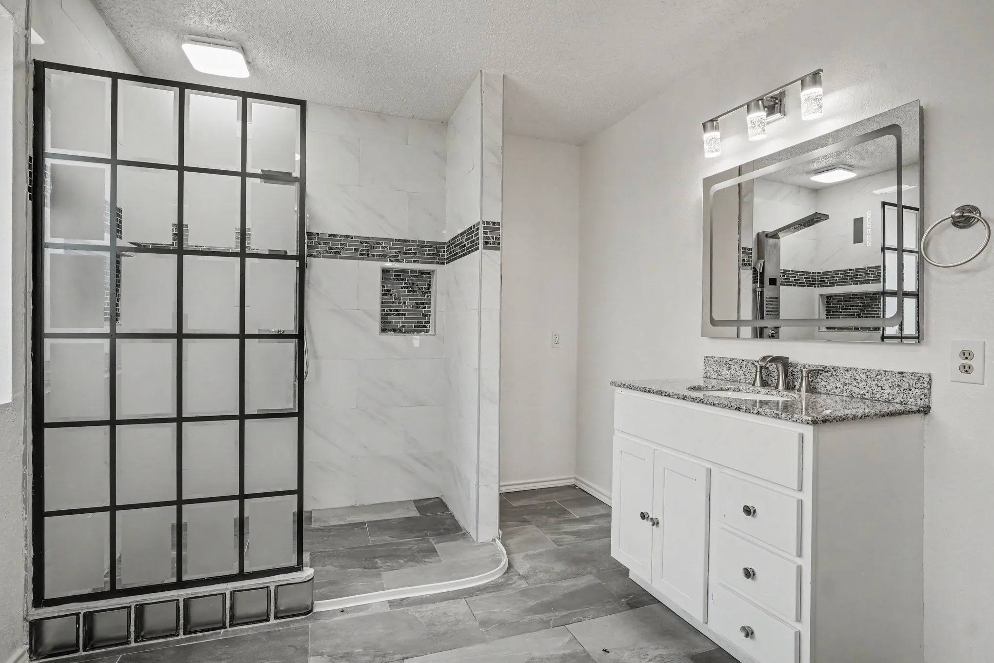 Walk-in shower with grid-patterned glass enclosure, white subway tile surround with mosaic accent, and built-in shower niche
