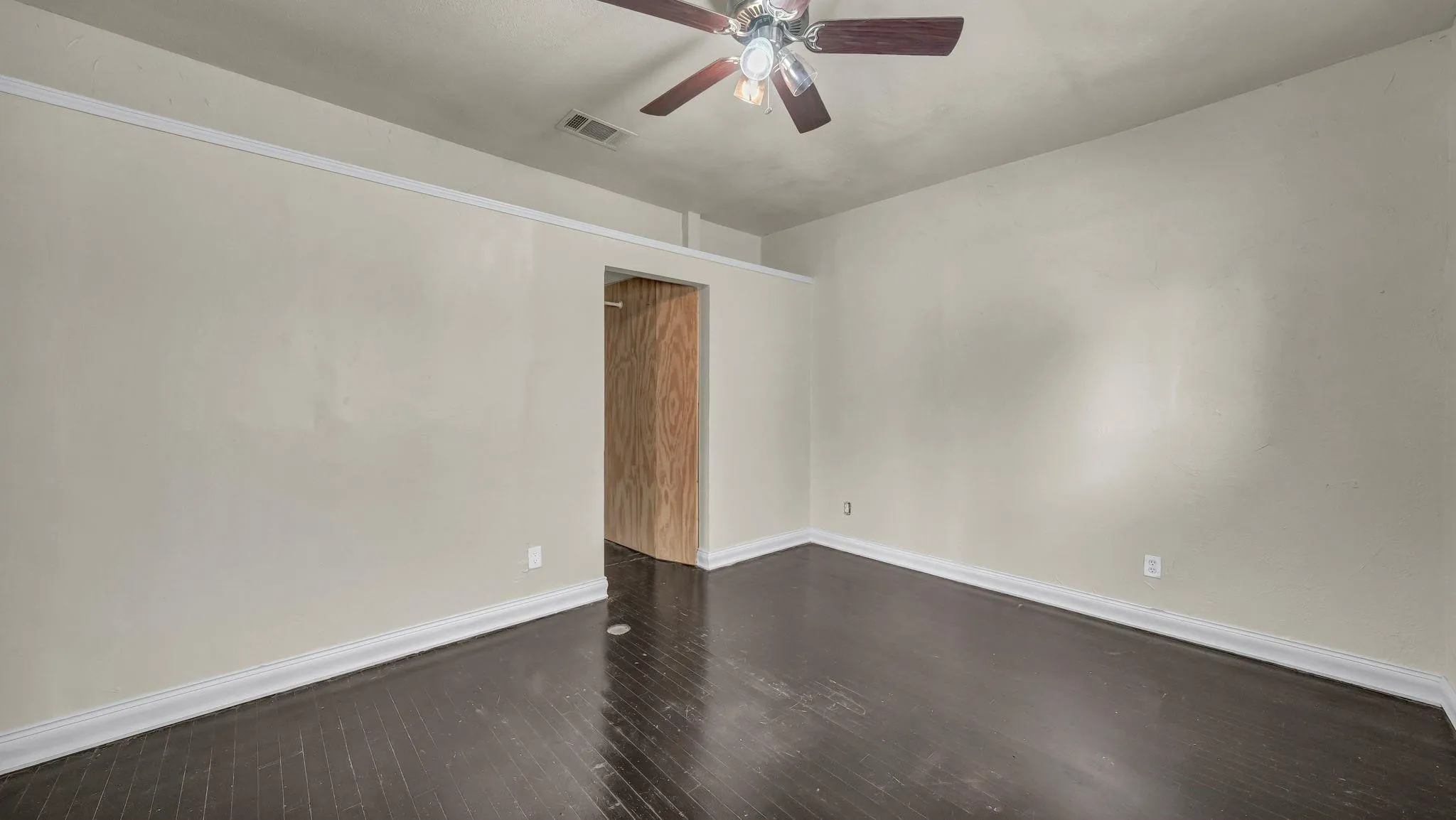 Spacious room featuring dark wood-finish flooring, light neutral-toned walls, and a ceiling fan with light fixture