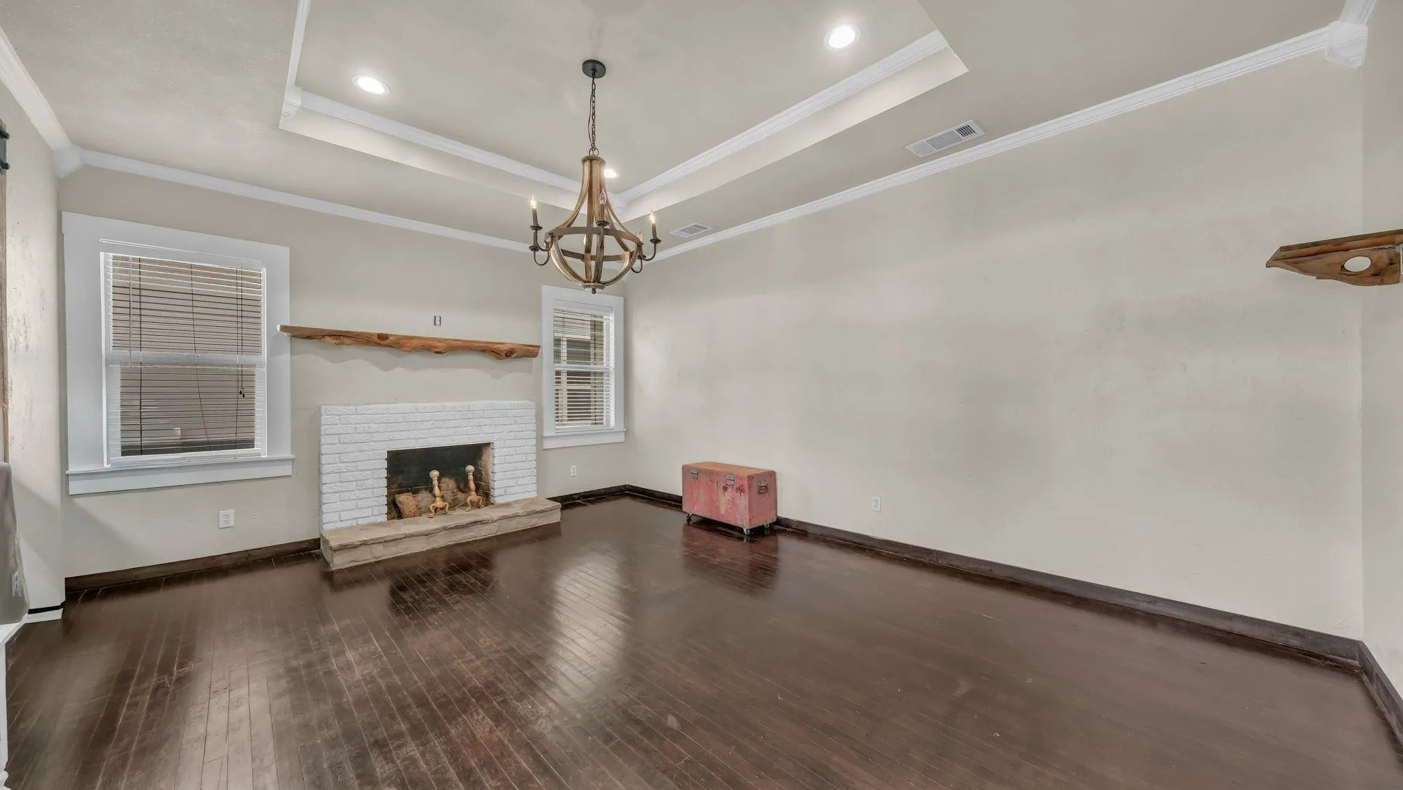 Dark wood-finish flooring with a white brick fireplace, rustic wood mantel, and wood chandelier