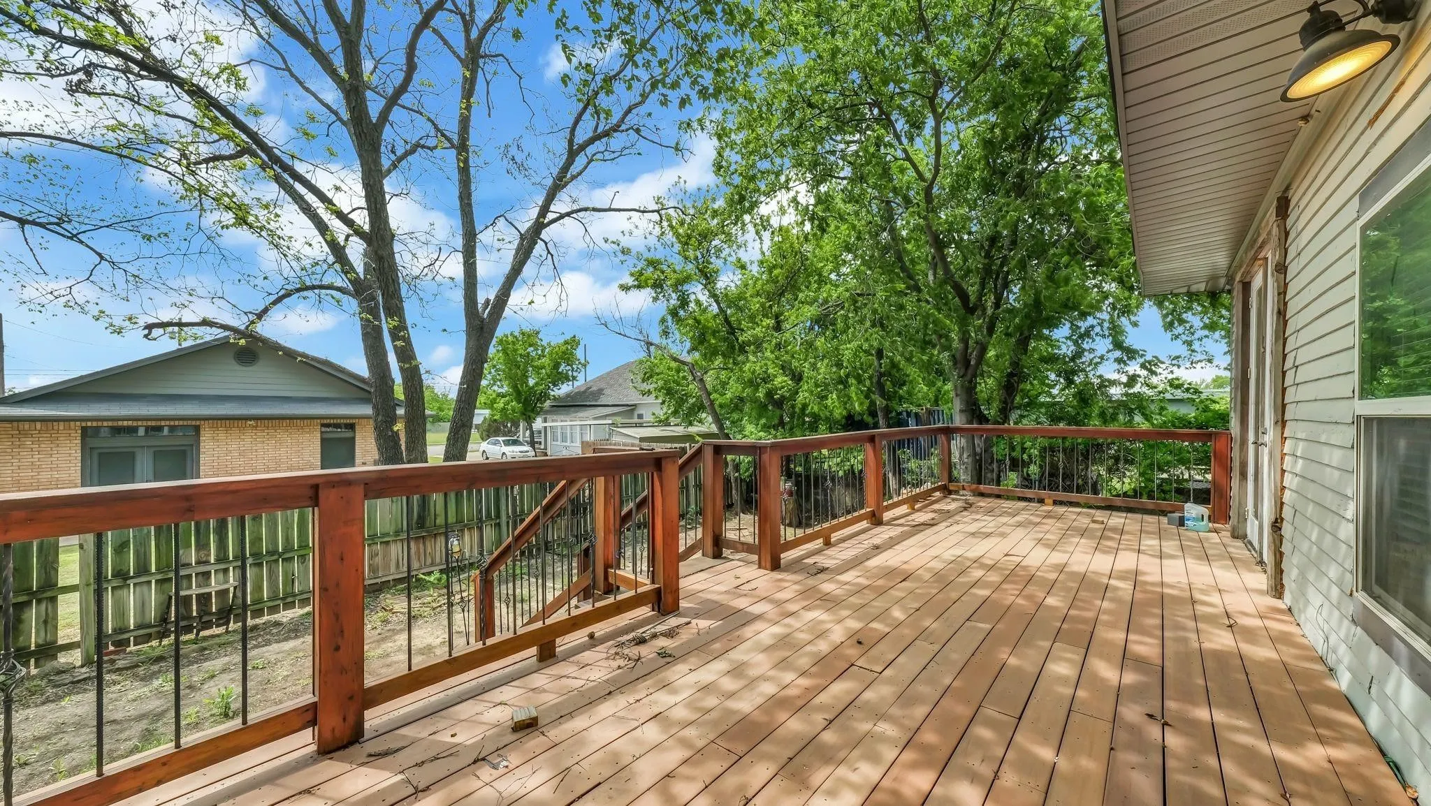 Expansive wood deck with wood and iron railings, white shiplap exterior siding, and exterior lighting fixture
